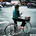 A woman reading SMS messages on her mobile phone while standing on a bike in traffic.