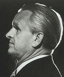 Black and white profile publicity shot of a clean-shaven man with strong features and greying hair, combed back