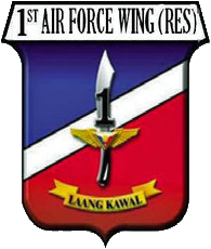 A shield-style crest primarily in red and blue, divided with a diagonal white bar. The centre contains an symbolic military knife with the number '1' covering its blade. The crest is headed by '1st Air Force Wing (Res)' in all-upper-case letters. Below the knife is a yellow banner for its motto containing the phrase 'Laang Kawal'.