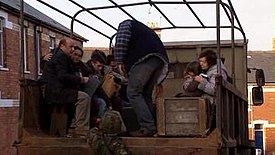 A family is taken away from their homes on the back of a truck.