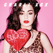 Charli XCX is holding a red heart shaped lollipop with the album's name on it, in a pink background.