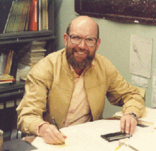 A photo of Dick Walker seated at his desk, holding papers and smiling.