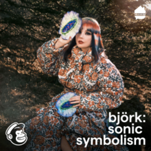 Björk sit outdoor while holding a crystal over her face.