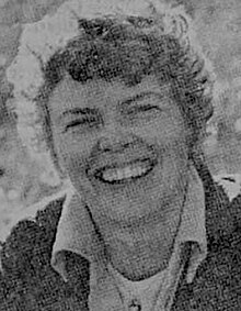 A smiling white woman with blond curly hair, photographed outdoors