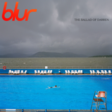 A photo of a swimming pool with a single swimmer surrounded by several chairs in the middle of a field surrounded by mountains.