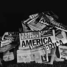 Cover art for "Delresto (Echoes)": a greyscale photo of a pile of newspapers; "The Echo" is the name of the newspaper; part of the headline reads "America" and the back of one newspaper has a picture of Beyoncé