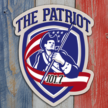 In a shield, a drawing of a Revolutionary soldier carrying a US flag with the words "The Patriot" arched over the top and "101.7" on the flag.