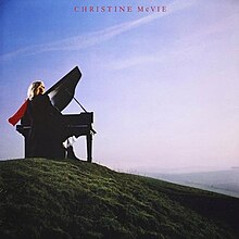 Cover of Christine McVie's 1984 album, showing McVie sitting behind a piano at the top of a green, grassy hill, looking to the right, toward the horizon