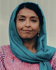 Woman wearing a turquoise sheila, a pink and blue dress and a golden earring smiling