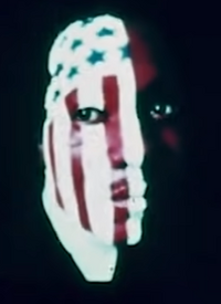 Color portrait of a Black man, serious expression, half his face painted in the manner of an American flag