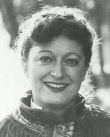 Black and white publicity photo of smiling woman wearing stage makeup, with hair tied back.