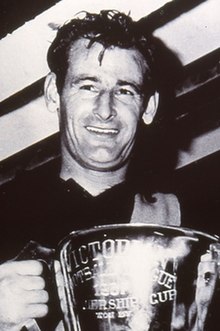 A smiling man holds a large silver trophy