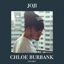 A photograph of Joji on a balcony wearing a black beanie and glasses, encompassed by a dark blue frame which features the project's title and Joji's name.