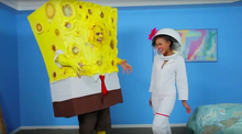 Still of Anthony Rosano in a large SpongeBob SquarePants costume and Chloe Addison in a smaller Sandy Cheeks one, both in a blue film set representing SpongeBob's bedroom.