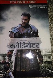 A man standing at the center of the image is wearing armor and is holding a sword in his right hand. In the background is the top of the Colosseum with a barely visible crowd standing in it. The poster includes the film's title, cast credits, and release date.